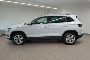 Vue de profil côté gauche d’un Skoda Karoq blanc Lune 2025 avec pack chrome extérieur et rampes de pavillon argent.