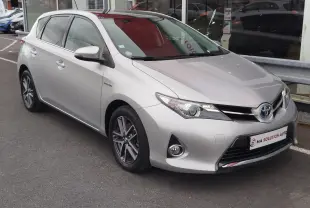 Toyota Auris HSD 136h gris aluminium vue 3/4 avant droit, avec jantes alliage et calandre distinctive hybride.