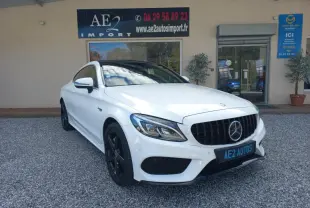 Vue 3/4 avant gauche d'une Mercedes Classe C Coupé blanche avec calandre noire et jantes noires, stationnée devant un garage.