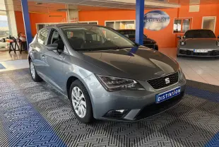 SEAT Leon gris vue 3/4 avant droit, garée en intérieur avec éclairage naturel et plaque Distinxion visible.