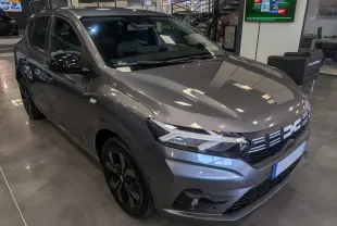 Vue 3/4 avant d'une Dacia Sandero TCe 90 gris schiste en showroom, avec jantes noires et calandre distinctive.