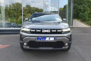 Vue avant d'un Dacia Duster 2026 gris schiste avec calandre noire et phares allumés, devant une vitrine de concession.