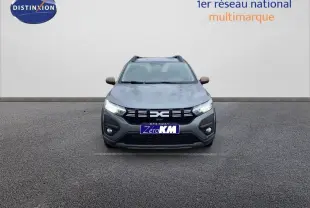 Vue frontale d'une Dacia Sandero Stepway gris schiste métal avec calandre noire et feux allumés sur fond neutre.