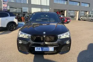BMW X4 30DA X DRIVE noir métal vu de face, avec calandre noire et phares LED allumés, sur parking extérieur.