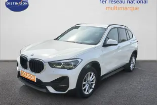 BMW X1 blanc vue 3/4 avant droit, avec calandre noire et jantes argentées sur fond neutre.