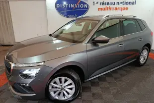 Vue 3/4 avant droit d’un Skoda Kamiq gris clair avec jantes alliage et barres de toit blanches en intérieur showroom.