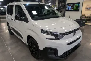 Vue 3/4 avant d'un Citroën Berlingo blanc Glacier avec jantes noires dans un showroom moderne.