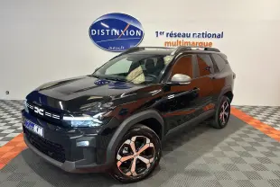 Dacia Bigster 2026 noir nacré en 3/4 avant droit, avec jantes bicolores et hayon électrique visible en arrière-plan.