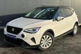 Vue 3/4 avant droite d'un SEAT Arona blanc avec toit noir et jantes alliage 16 pouces, stationné devant un mur gris.