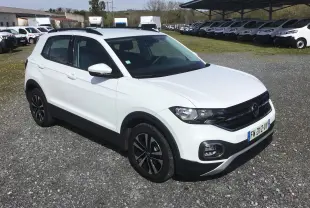 Volkswagen T-Cross blanc vue 3/4 avant droit, avec jantes noires et toit ouvrant, stationné sur un sol gravillonné.