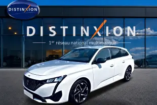 Peugeot 308 SW blanche vue en 3/4 avant droit, avec jantes alliage noires et toit vitré, devant une vitrine Distinxion.