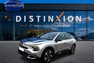 Citroën C4 gris en 3/4 avant droit, avec jantes alu et calandre distinctive, devant une vitrine de concession.