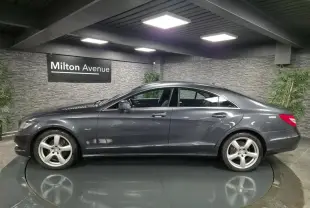 Profil côté gauche d'une Mercedes CLS 250 CDI gris métallisé avec jantes alliage 5 branches en intérieur showroom.