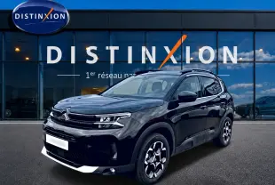 Citroën C5 Aircross noir vue 3/4 avant droit, avec jantes alu et barres de toit visibles devant une vitrine Distinxion.