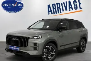 Vue 3/4 avant du SUV JAECOO J7 gris olive avec toit noir et calandre verticale distinctive, en intérieur showroom.
