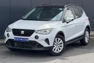 Vue 3/4 avant droite d'un SEAT Arona blanc alpin avec toit noir et jantes alliage 16 pouces, sur fond urbain.