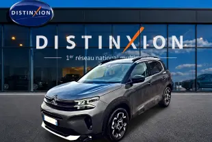 Citroën C5 Aircross gris en 3/4 avant droit, avec jantes alu et barres de toit visibles devant showroom Distinxion.