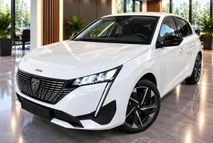 Peugeot 308 blanc okenite vue 3/4 avant droit, avec calandre noire distinctive et jantes alliage bicolores.