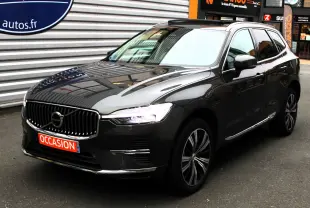 Volvo XC60 gris épicéa métallisé en 3/4 avant droit, avec calandre verticale et feux LED allumés.