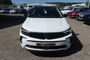 Vue avant d'un Opel Grandland blanc métallisé avec calandre noire brillante sur un parking extérieur.