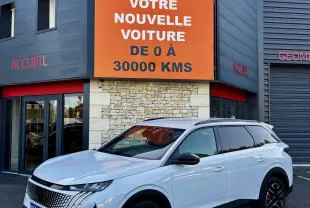 Peugeot 5008 blanc vue 3/4 avant droit, avec jantes noires et calandre distinctive, devant un bâtiment commercial.