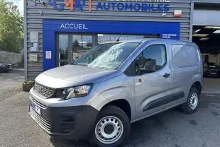Vue 3/4 avant droit d'un Peugeot Partner Dangel 4x4 gris Artense avec protections noires et jantes acier devant un garage.