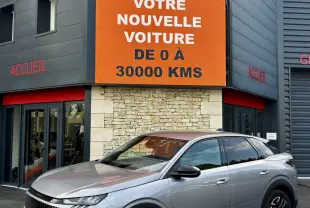 Peugeot 3008 gris clair vue 3/4 avant droit, avec calandre distinctive et jantes noires, devant un bâtiment commercial.