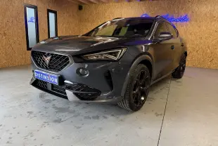 Vue 3/4 avant d'une CUPRA Formentor gris clair 2023 avec jantes noires et logo cuivré, en intérieur showroom.