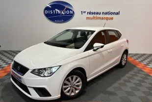 SEAT Ibiza blanc vue 3/4 avant droit en intérieur, avec phares allumés et jantes alliage simples.