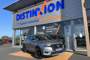 DS7 gris Artens en 3/4 avant droit, avec calandre noire distinctive et jantes noires brillantes, devant un showroom Distinxion.