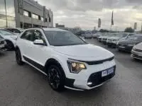 KIA Niro EV blanc 2024 en 3/4 avant droit, avec signature lumineuse distinctive et jantes noires contrastantes.