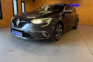 Renault Mégane Break GT gris vue 3/4 avant droit, phares allumés, dans un intérieur avec murs en bois.