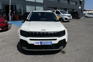 Vue avant d’un Jeep Avenger blanc électrique 2025 avec calandre noire et plaque « Véhicules Occasions » sur parking.