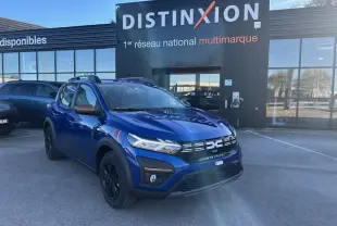 Dacia Sandero III Stepway bleu Iron en 3/4 avant droit, avec calandre noire et barres de toit brun cuivré.