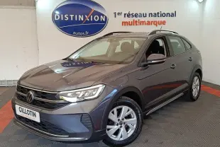 Volkswagen Taigo gris foncé en 3/4 avant droit dans un showroom avec logo Distinxion en arrière-plan.