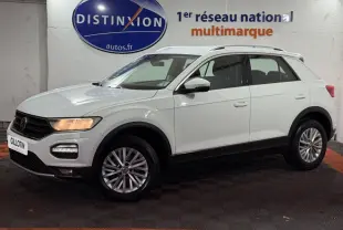 Volkswagen T-Roc blanc en vue de profil côté gauche, avec jantes alliage et barres de toit noires visibles.
