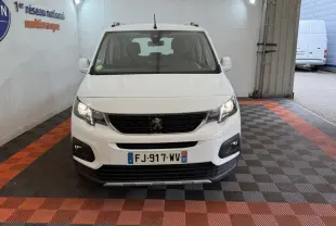 Vue frontale d'un Peugeot Rifter blanc 2019 avec calandre noire et feux allumés dans un garage.