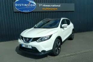 Nissan Qashqai blanc vue 3/4 avant droit, avec toit noir et jantes alliage noires, stationné devant un mur sombre.