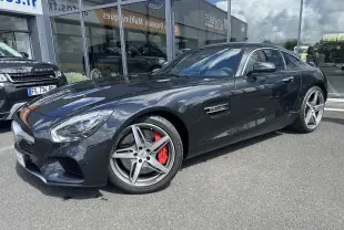 Mercedes AMG GT gris foncé vue 3/4 avant droit, avec jantes cinq branches et étriers de frein rouges visibles.