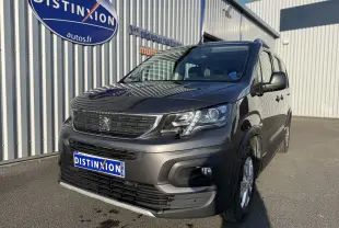 Peugeot Rifter gris platinium en 3/4 avant droit, avec calandre noire et jantes alliage visibles, stationné devant un bâtiment.