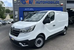 Renault Trafic Fourgon blanc en 3/4 avant droit, avec calandre noire et projecteurs modernes, stationné devant un garage.