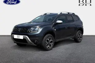 SUV Dacia Duster gris Comète métallisé vu en 3/4 avant droit avec barres de toit et jantes alu noires.
