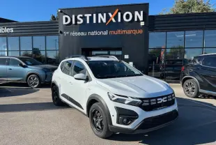 Dacia Sandero Stepway blanc arctique vue 3/4 avant avec calandre noire et barres de toit noires devant un showroom.