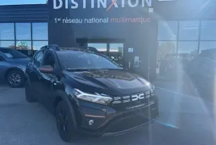 Vue 3/4 avant d'une Dacia Sandero Stepway noire nacrée avec calandre et rétroviseurs brun cuivré, stationnée devant un bâtiment.