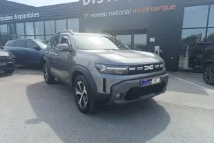 Vue 3/4 avant droit du Dacia Duster 2026 gris schiste métal avec jantes alliage et barres de toit noires.