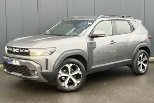 Dacia Duster gris schiste en 3/4 avant droit, avec jantes alliage diamantées et barres de toit noires.