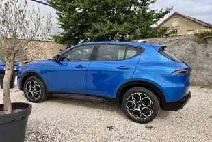 Vue de profil côté gauche d'un Alfa Romeo Tonale 1.5 mHEV Sprint bleu métallisé garé sur gravier, avec jantes distinctives.