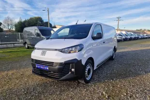 Fourgon FIAT Scudo blanc en 3/4 avant droit, avec pare-chocs noirs et jantes acier, stationné sur un terrain gravillonné.