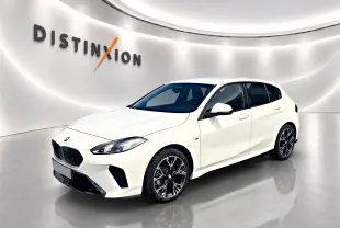 BMW Série 1 blanche vue en 3/4 avant droit, avec jantes alliage noires et calandre M sport dans un showroom lumineux.