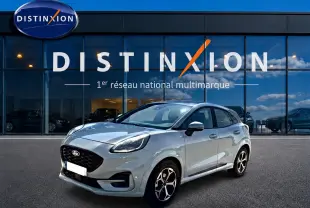 Ford Puma gris cactus en 3/4 avant droit, avec jantes alu et calandre noire, devant une vitrine Distinxion.
